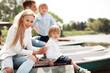 © Eva March - Family of four - parents and two twin boys sitting on pier near boats outdoors in park in sunny weather. Celebrating holidays and happy time together. Outdoor family activity, leisure time together