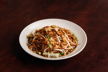 Canvas Print - Closeup shot of a Fried Bee Hoon (Singapore Noodles), in a white plate on a brown wooden table