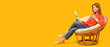 © Pixel-Shot - Beautiful woman drinking coffee and reading newspaper while sitting in cozy armchair against yellow background with space for text