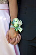 Closeup up shot of a couple holding hands with a wrist corsage at their prom with blurred background