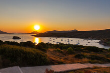 Sunset In  Lavrio Bay. The Red And Yellow Glowing Sun Sinks On The Horizon. Boats Anchor And Lie Off The Coast. Romantic Scene In The Cyladen Archipelago In The Aegean Sea. Sunset At The Sea