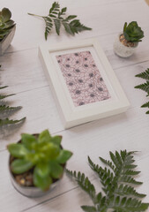 Wall Mural - Vertical high angle shot of a picture frame on a wooden surface surrounded with plants and cactuses