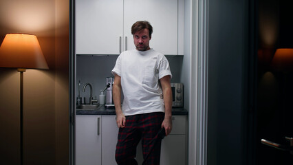 Sleepy man in pajamas standing in kitchen early in morning