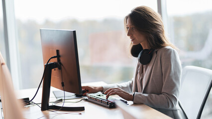 Focused businesswoman with headphones working on computer at workplace in modern office