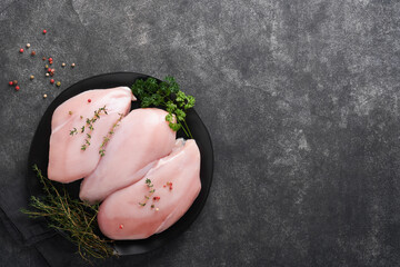 Wall Mural - Chicken breast. Raw chicken breast fillets on black ceramic plate on wooden cutting board with herbs and spices on black background. Top view with copy space.