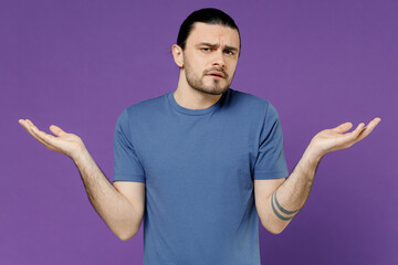 Wall Mural - Young man 20s in basic blue t-shirt with blank print design spread hands shrugging shoulders looking puzzled, have no idea isolated on plain purple background studio portrait People lifestyle concept