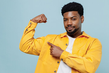Wall Mural - Young strong sporty fitness man of African American ethnicity 20s in yellow shirt showing biceps muscles on hand demonstrating strength power isolated on plain pastel light blue background studio.