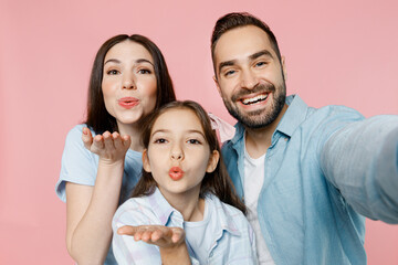 Wall Mural - Close up young happy lovely parents mom dad with child kid daughter teen girl in blue clothes doing selfie shot pov on mobile cell phone blow air kiss isolated on plain pastel light pink background