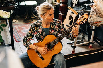 A woman sitting on the floor on a small rehearsal stage plays the acoustic guitar.