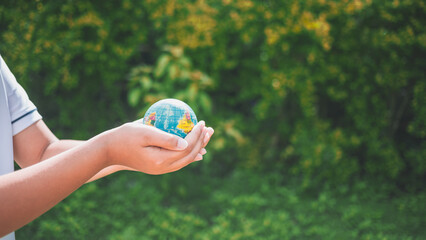 Planet earth in the boy's hands saves and protects the world over blurred green nature background. Environmental concept on Earth Day.