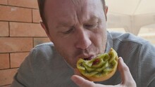 An Adult Unshaven Caucasian Man Bites Off A Cake With Kiwi Slices. Slow Motion.