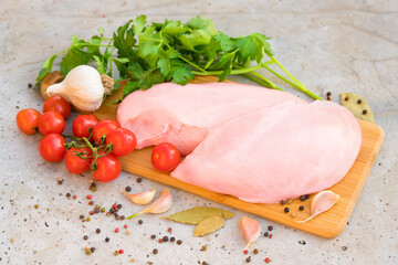 Fresh raw chicken fillet with herbs, spices and tomatoes on wooden cutting board. Uncooked chicken breast on concrete table background. Food background