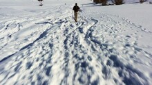 Man In Khaki-colored Hiking Pants And Black Polo Does Nordic Walking In His Mountain Boots In A Thick Layer Of Snow In Mount Hermon In Israel On A Sunny Day. Quick Drone Tilt Shot