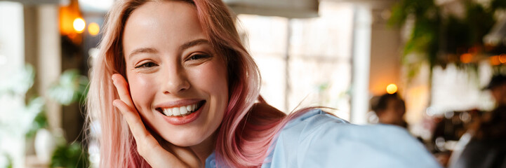 Wall Mural - Young woman with pink hair smiling and taking selfie photo in cafe