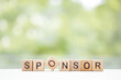 SPONSOR - word is written on wooden cubes on a green summer background. Close-up of wooden elements.