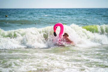 Wall Mural - Pink inflatable flamingo. A girl is swimming in the sea. Sea waves. Cheerful mood. Vacation at the sea.