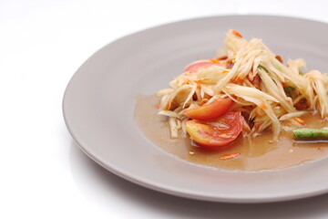 Thai papaya salad on a plate, papaya salad with poop, lime, pepper, red tomatoes in a gray plate on a white table.