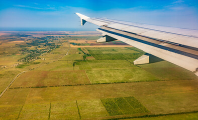 View of airplane wing, blue skies and green land during landing. Airplane window view.