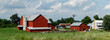 Red Amish Farm Buildings among green fields under a cloudy blue sky in Holmes County, Ohio