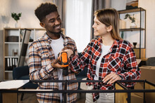 African American Man And Caucasian Woman Smiling To Each Other While Making Furniture Installation At New Flat. Happy Young Family Improving Interior At Their Own Home.