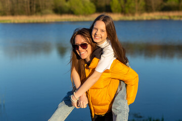 Wall Mural - Playful mother giving daughter piggy back ride at spring lake shore.