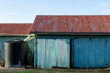 Corrugated Iron Farm Shed Painted Blue, With Red Roof, And Water Tank.