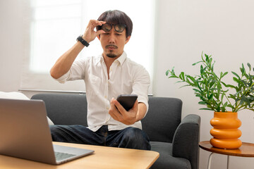 Wall Mural - Middle age Asian man squint eye to look at the phone due to long eye sighted problems, which makes vision difficult.