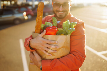 Wall Mural - Young man with shopping bag full of vegetables near the car. Handsome man  after shopping.