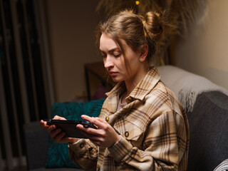 Wall Mural - A fair-haired girl plays a video game on a console at home in a room in the evening. Recreation, relaxation, hobby, strategy games, virtual reality, games with friends online. Profile shot.