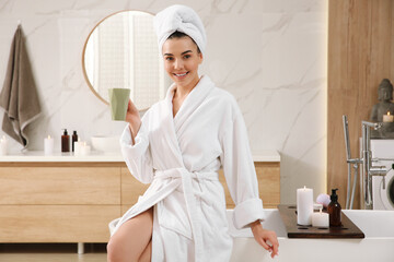 Sticker - Beautiful young woman with cup sitting on edge of tub in bathroom