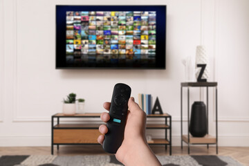 Wall Mural - Woman with remote control changing channels while watching TV at home, closeup