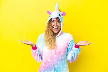 Wall Mural - Girl with curly hair wearing a unicorn pajama isolated on yellow background with shocked facial expression