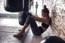 Side View Of Tired Caucasian Young Female Boxer Wearing Gloves Sitting By Brick Wall In Health Club