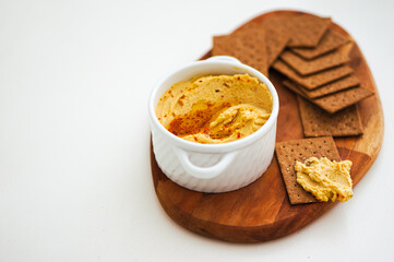 Selective focus top view of healthy homemade hummus with olive oil and red pepper with brown crackers on a wooden plate. Copy space for text layout. 