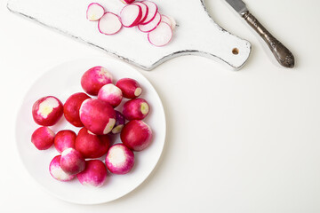 Red fresh radish in a white plate on a white table and chopped radish on a cutting board