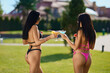 Sexy brunette woman in g-strings bikini enjoying tasty drinks at resort outdoor. Back view of attractive long haired female friends celebrating with fresh cocktails on vacation. Concept of relaxation.