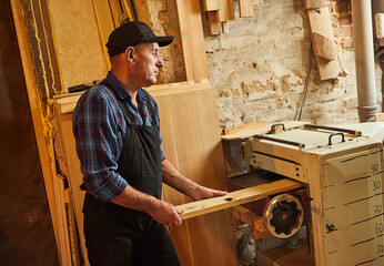 Wall Mural - Senior carpenter in uniform works with a wood on a woodworking machine at the carpentry manufacturing 