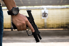 A Gun Shooter Holds 9mm Automatic Pistol In Right Hand In Front Of The Gun Shooting Range, Concept For Security, Robbery, Gangster And Bodyguard Training Around The World. Selective Focus On Pistol.