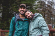 © Samuel Ponce - Two happy, young, caucasian, bearded and handsome brothers with jacket, cap and backpacks in a wooden bridge in the forest in a rainy day, Valdivia, Chile