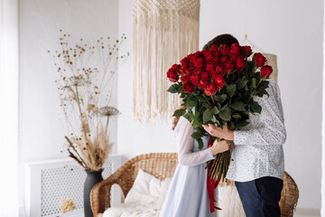 Wall Mural - couple in love of man and woman kissing behind big red roses bouquet at home. happy valentines day. engagement day.