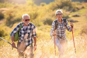 Active senior Caucasian couple hiking in mountains with backpacks and hiking poles, enjoying their adventure