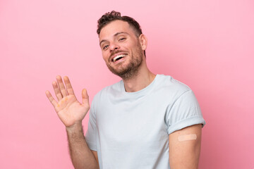 Wall Mural - Young Brazilian man wearing a band-aids isolated on pink background saluting with hand with happy expression