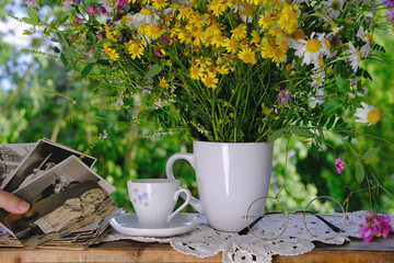 female hands going through old photos of 40s, 50s, bouquet of wildflowers, handmade lacy, cup of tea on table in garden, concept of genealogy, memory of ancestors, family tree, family archive