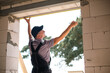 © Ольга Симонова - Construction worker at construction site measures the length of window opening and brick wall with tape measure. Cottage are made of porous concrete blocks, work clothes - jumpsuit and baseball cap