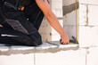 © Ольга Симонова - Construction worker at construction site measures the length of window opening and brick wall with tape measure. Cottage are made of porous concrete blocks, work clothes - jumpsuit and baseball cap