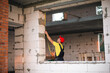 © Ольга Симонова - Construction worker at construction site measures the length of window opening and brick wall with tape measure. Cottage are made of porous concrete blocks, work clothes - jumpsuit and baseball cap