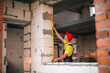 © Ольга Симонова - Construction worker at construction site measures the length of window opening and brick wall with tape measure. Cottage are made of porous concrete blocks, work clothes - jumpsuit and baseball cap
