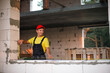 © Ольга Симонова - Construction worker at construction site measures the length of window opening and brick wall with tape measure. Cottage are made of porous concrete blocks, work clothes - jumpsuit and baseball cap