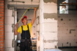 © Ольга Симонова - Construction worker at construction site measures the length of window opening and brick wall with tape measure. Cottage are made of porous concrete blocks, work clothes - jumpsuit and baseball cap