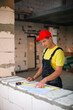 © Ольга Симонова - Construction worker at construction site measures the length of window opening and brick wall with tape measure. Cottage are made of porous concrete blocks, work clothes - jumpsuit and baseball cap